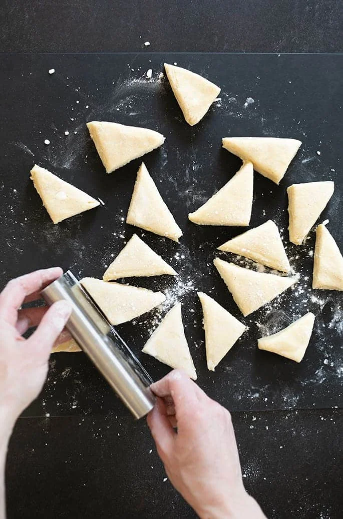 Hands cutting triangles of dough.