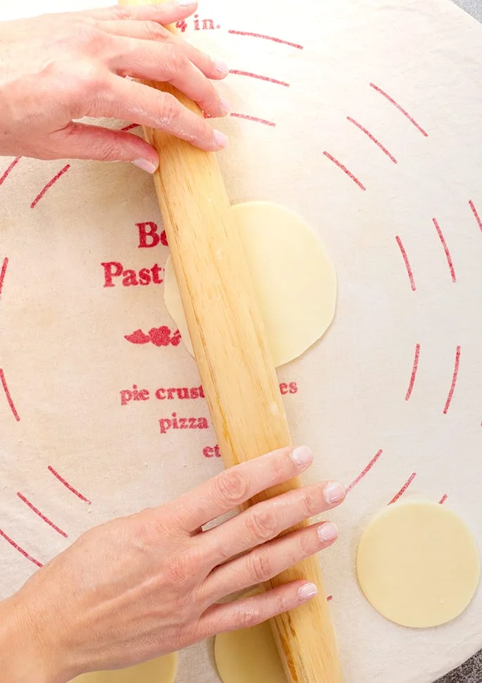 Hands holding rolling pin rolling out rounds of dough