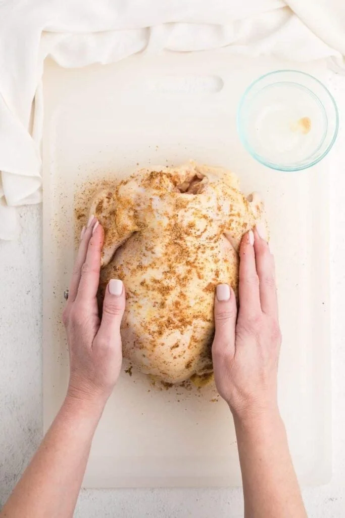 Hands on both sides of the raw whole chicken placing seasoning on it