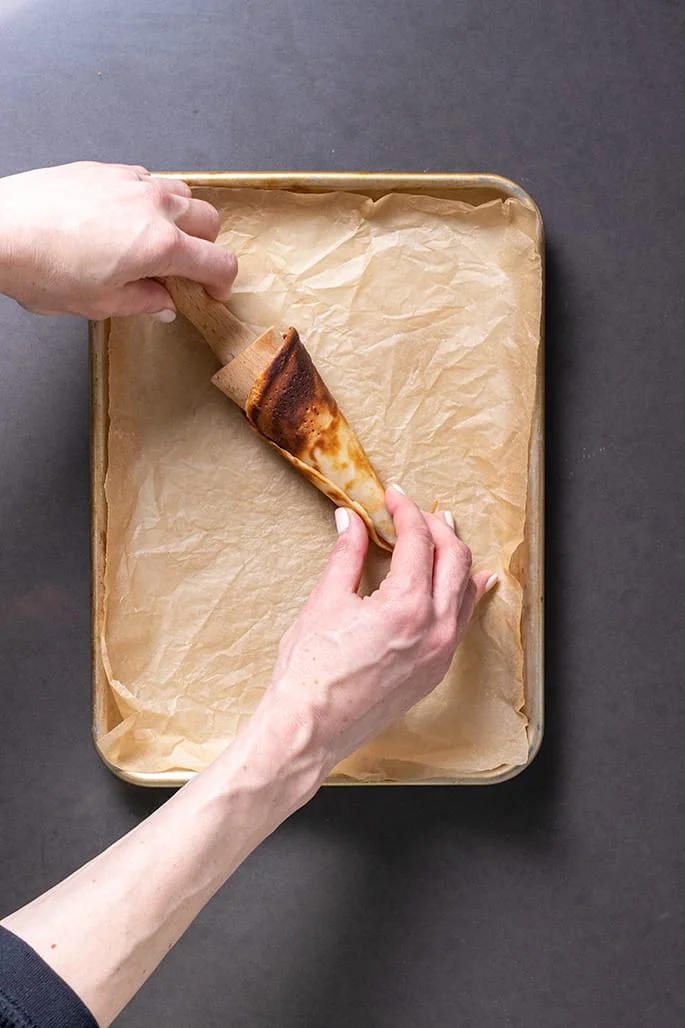 Hands rolling cone pancake onto wooden cone with handle
