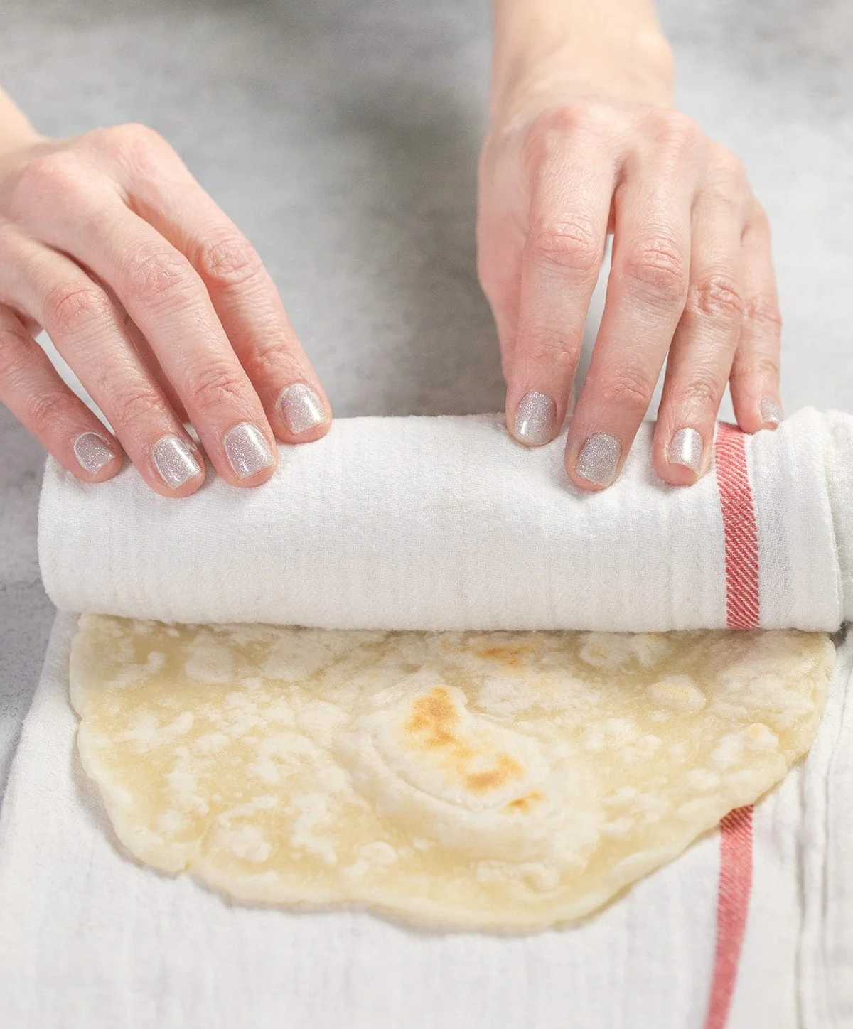Hands rolling flatbread in a white towel with a red stripe
