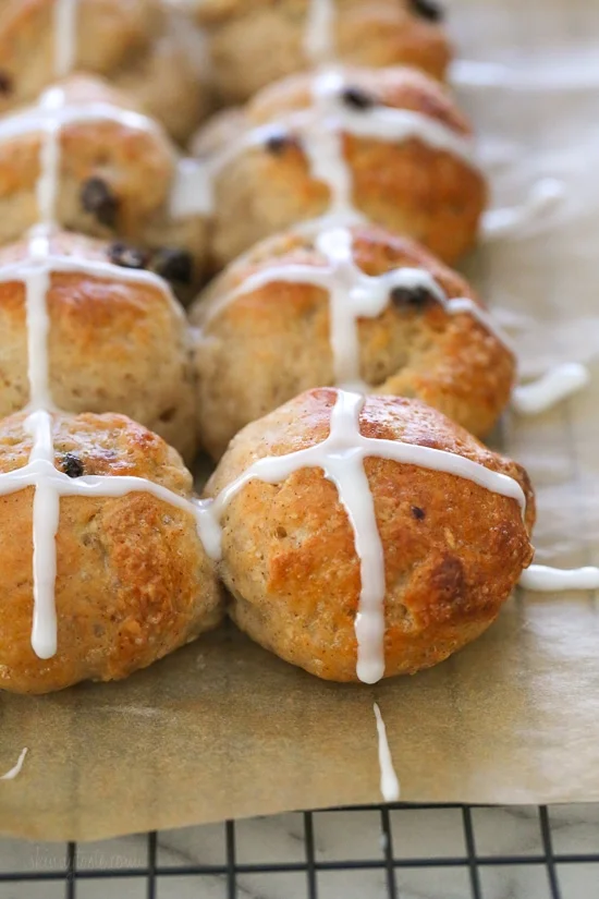 Homemade hot cross buns topped with icing on a parchment-lined rack.