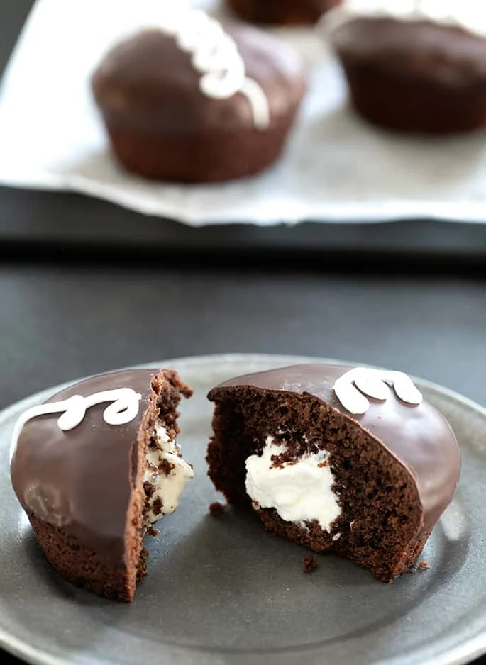 Hostess-style gluten free chocolate cupcake on a plate, split in half to show cream filling.