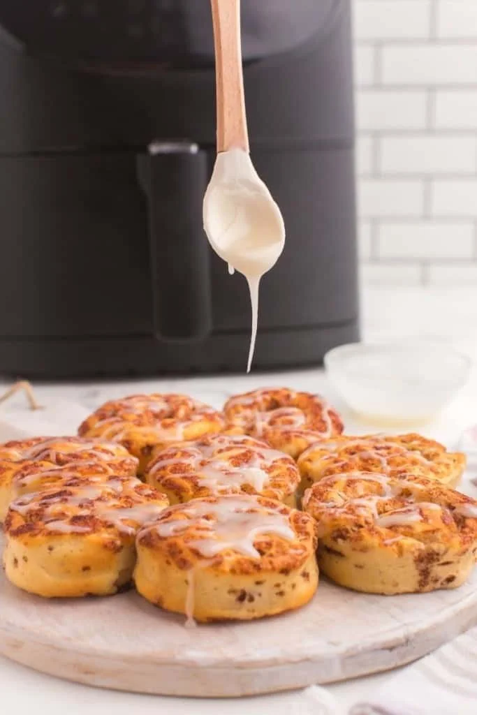 Icing being dripped onto cooked cinnamon rolls in front of an air fryer