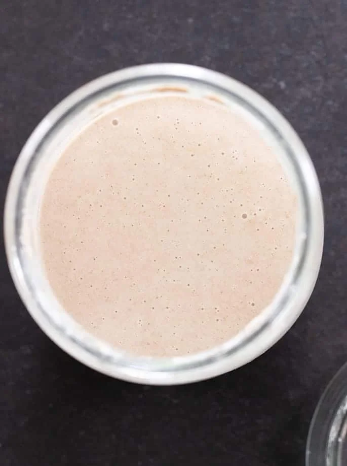 image from above of light brown liquid with small bubbles in it in glass jar on black surface
