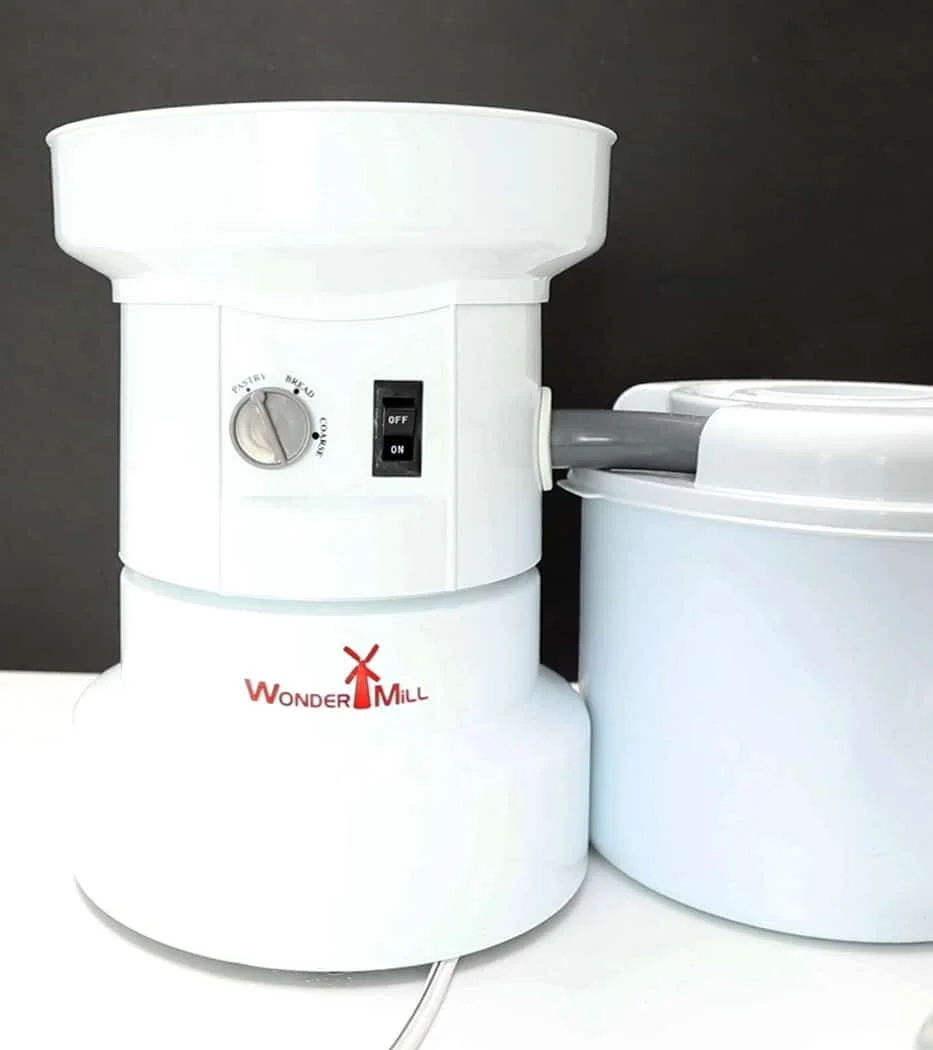 Image of a WonderMill grain mill in the on position set up on a white table with a black background
