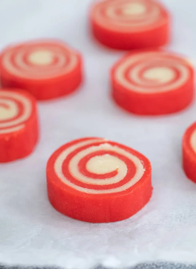 Individual raw red and white pinwheel cookies on white paper.