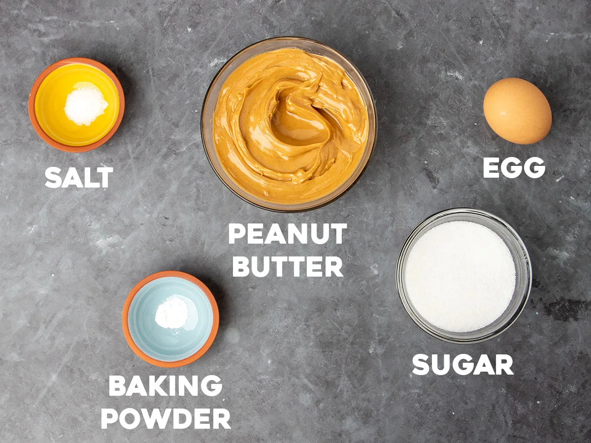 ingredients for flourless peanut butter cookies in small bowls with white block writing with names of ingredients
