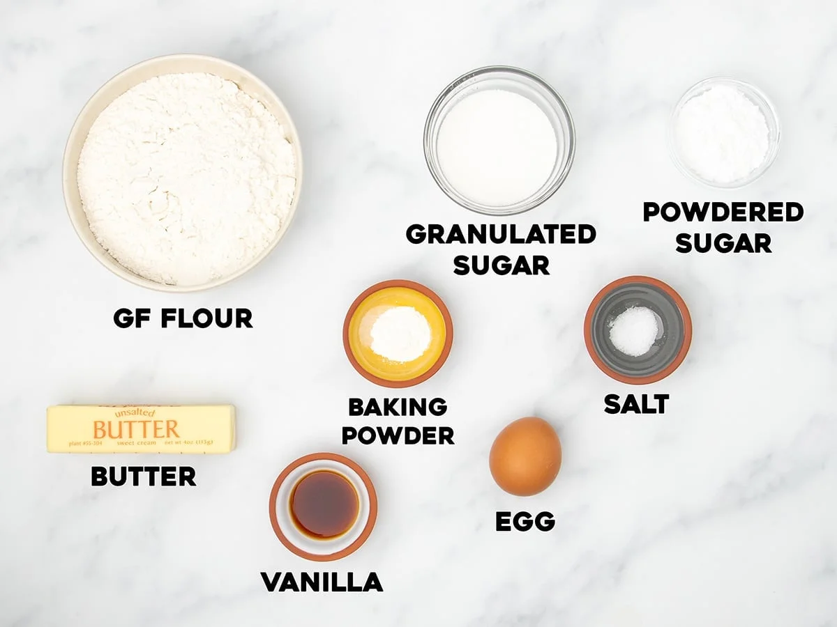 Ingredients for the cookies in small bowls on marble surface with black block letters with name of each ingredient.