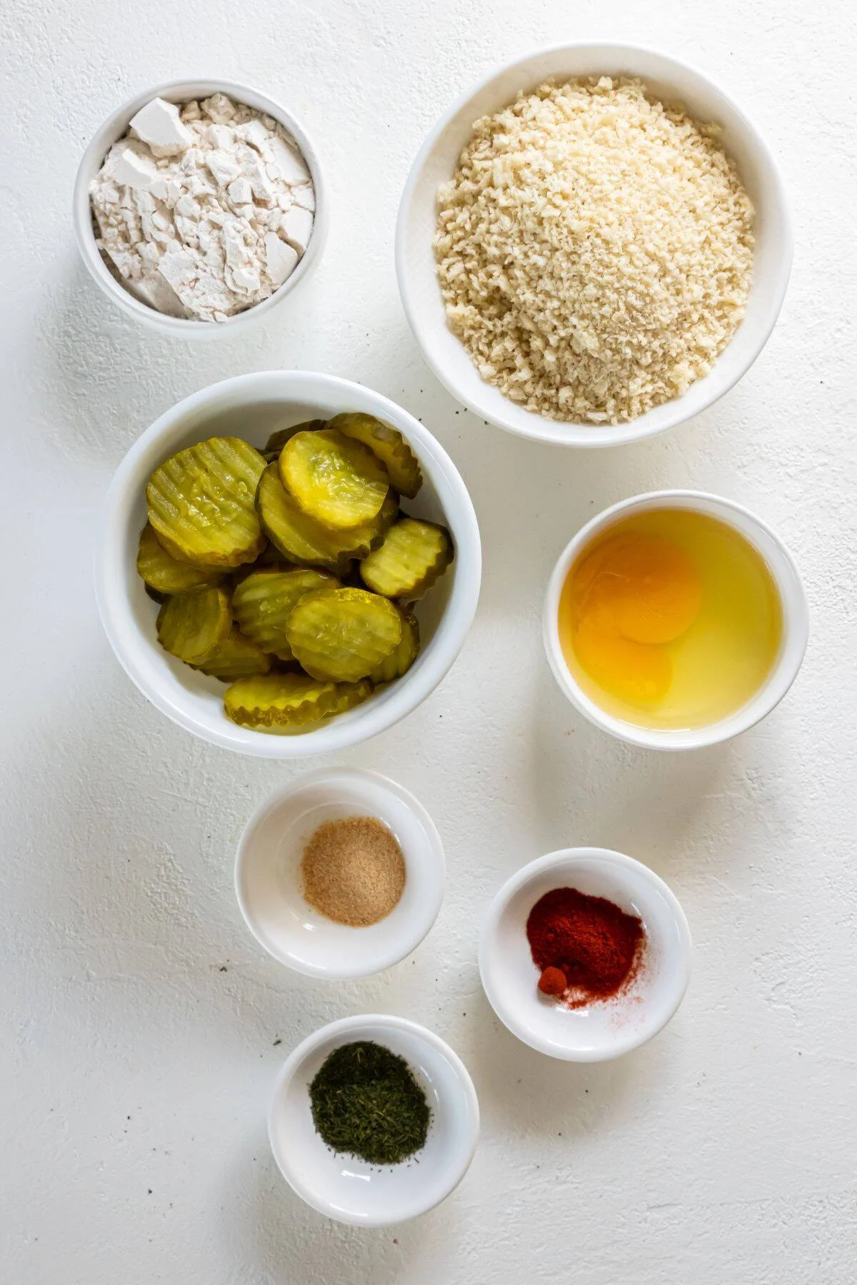 Ingredients needed to make air fryer fried pickles: pickles, breadcrumbs, egg, water, flour, garlic powder, paprika, and dried dill.