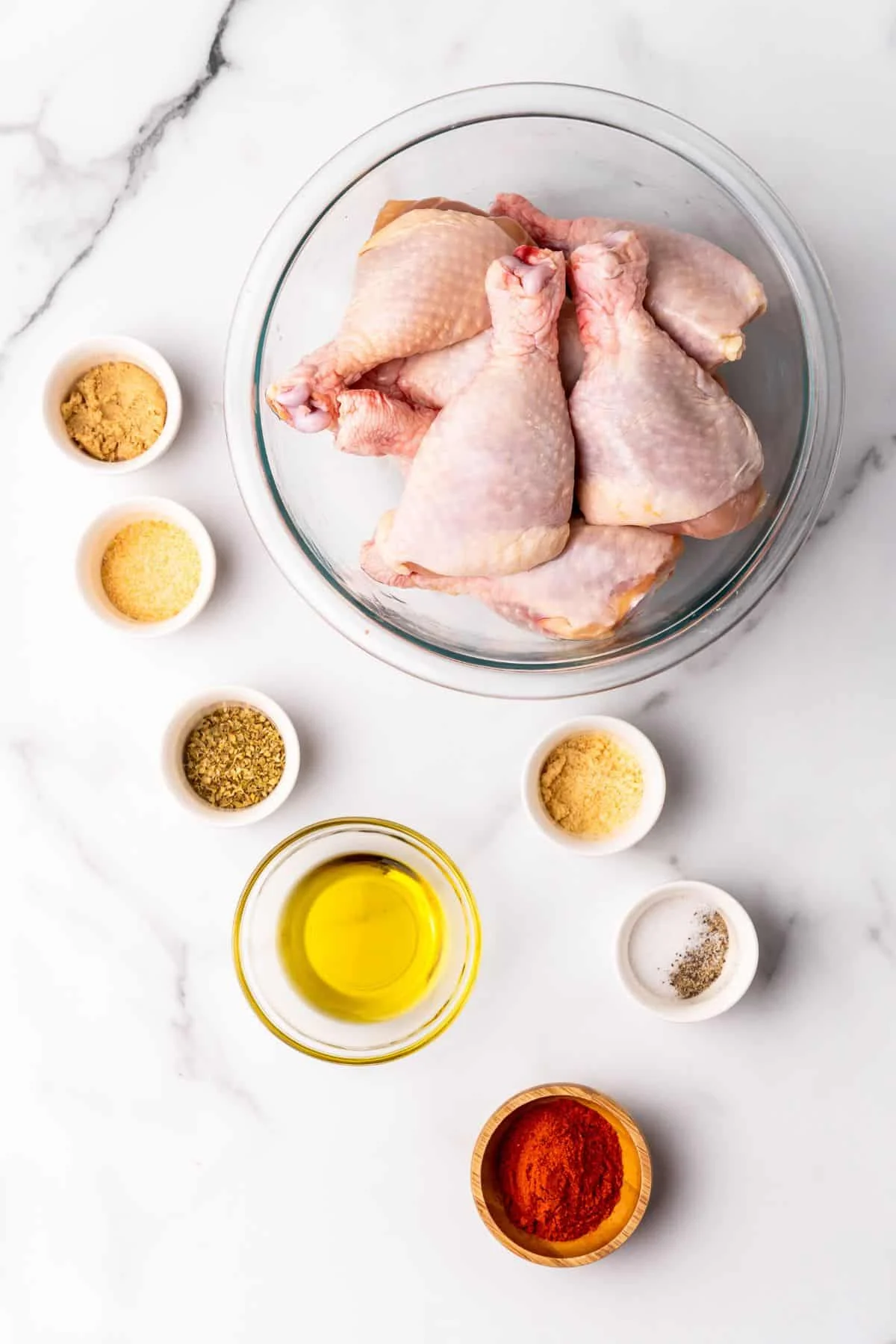 Ingredients needed to make chicken legs in the air fryer: chicken legs, oil, and seasonings in separate bowls.