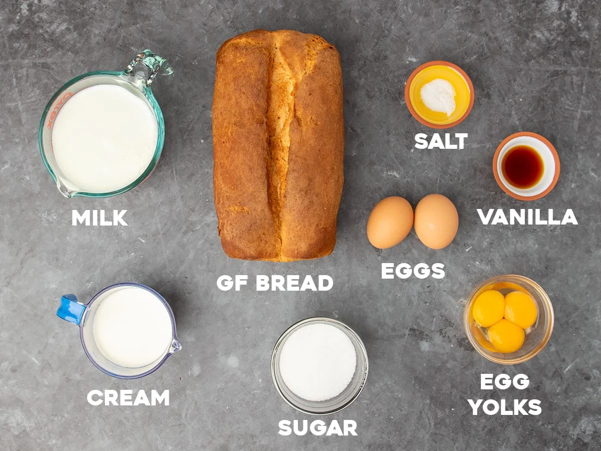 ingredients to make gluten free bread pudding in small bowls on black marble surface with white block letters with the names of the ingredients