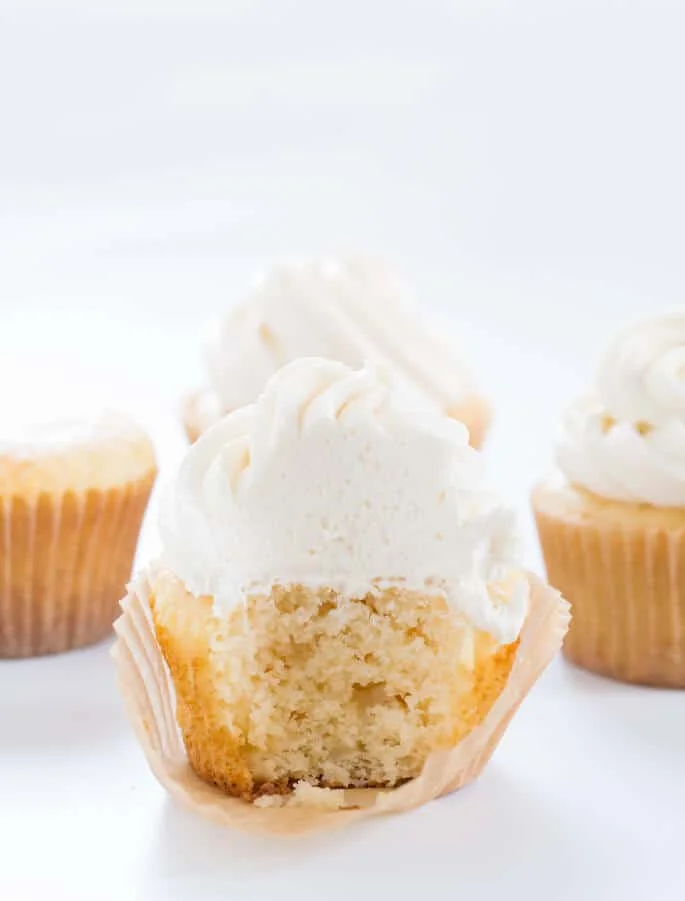 Inside view of vanilla cupcake with 3 other vanilla cupcakes in back on white surface 