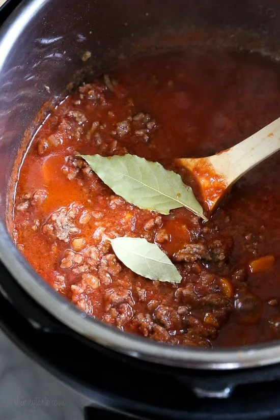 Instant Pot bolognese sauce inside the pressure cooker, with bay leaves next to a wooden spoon.