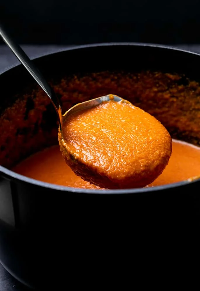 Ladleful of tomato soup in black stockpot
