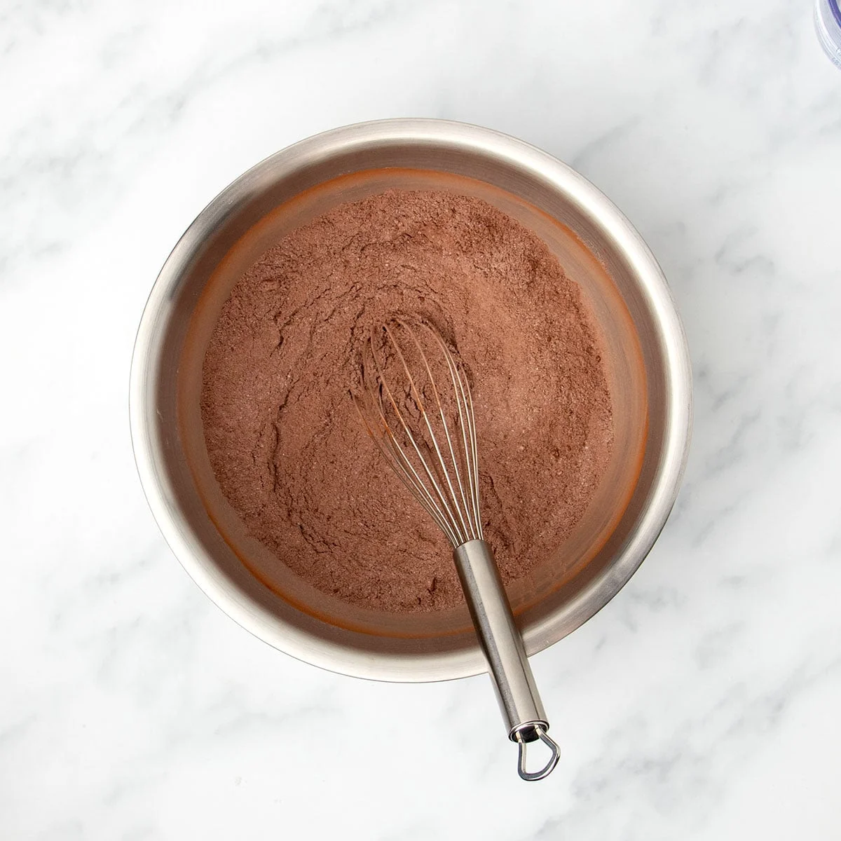 Large round metal mixing bowl with brown powder and metal wire whisk