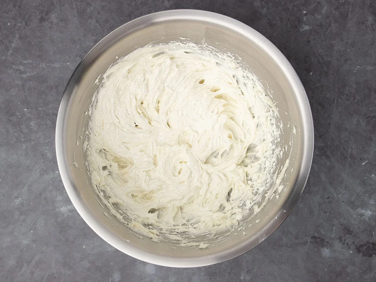 large round metal mixing bowl with whipped white cream cheese frosting with black flecks from vanilla seeds