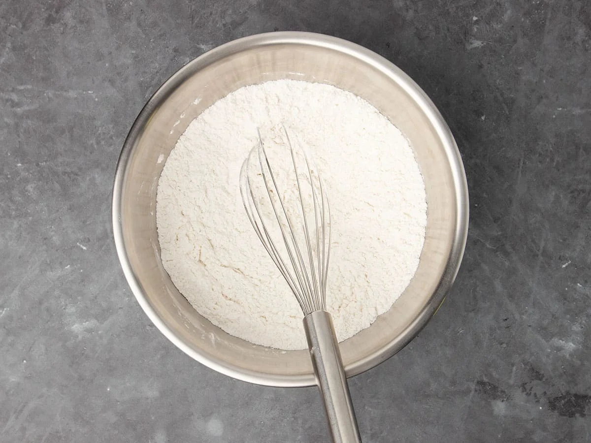 large round metal mixing bowl with white flour and a large metal wire whisk
