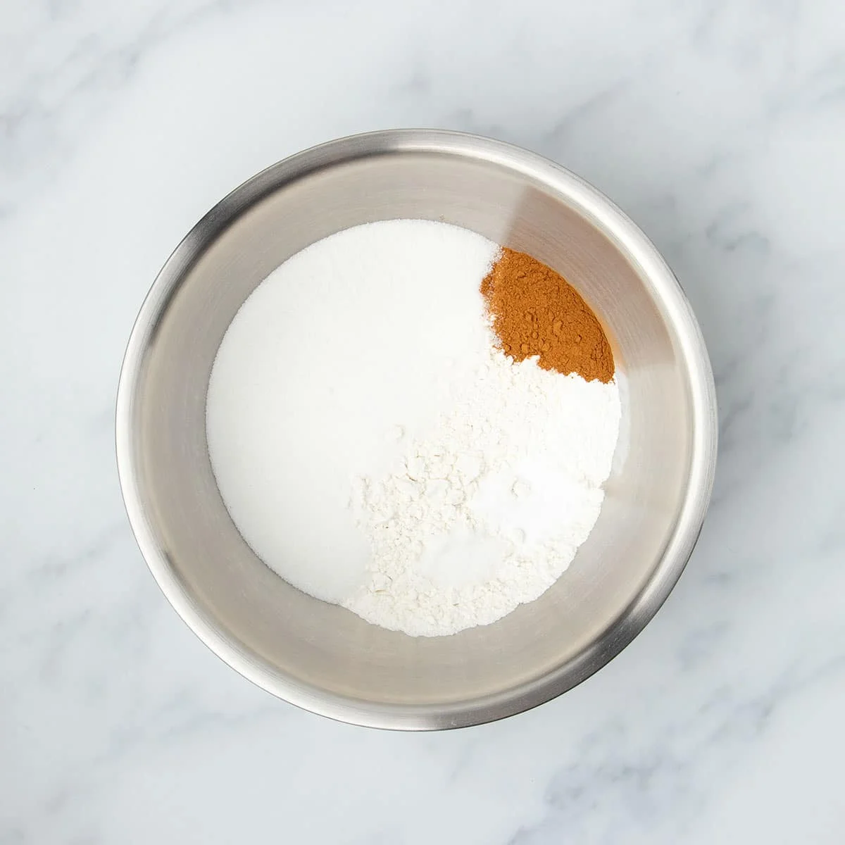 Large round metal mixing bowl with white powders and some brown cinnamon powder.