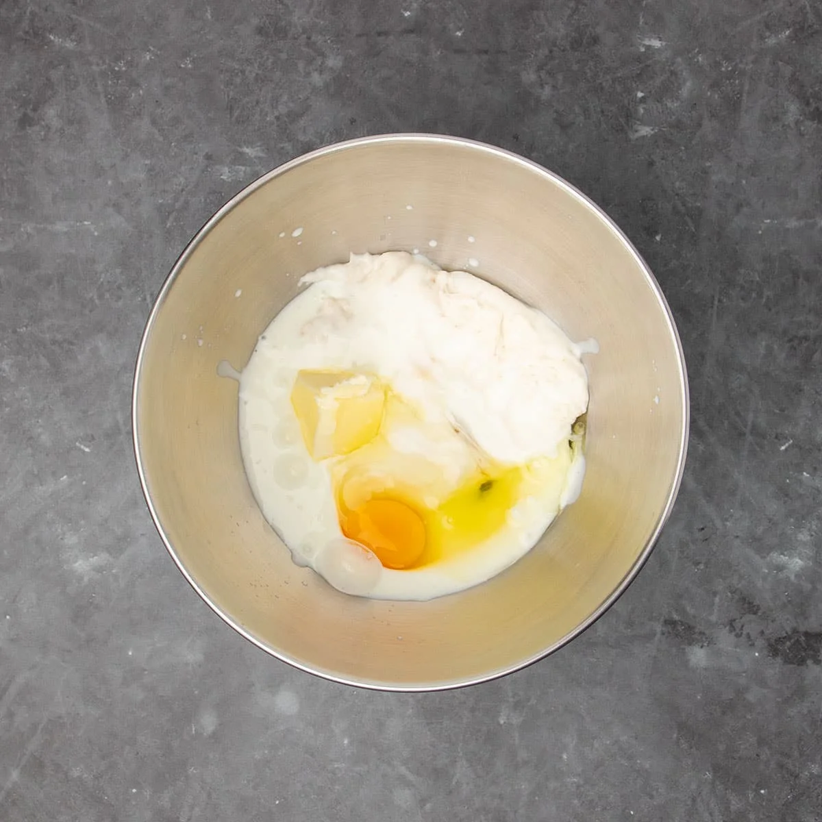 large round metal stand mixer mixing bowl with white risen starter, white milk, yellow egg and yellow butter