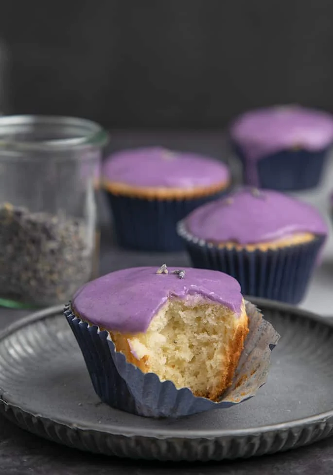 Lavender glazed cupcake with bite taken on metal plate.