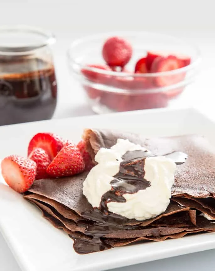 Learn how to make chocolate gluten free crêpes with this easy recipe. Fill with fresh whipped cream and drizzle with chocolate sauce for the perfect showstopper dessert! 