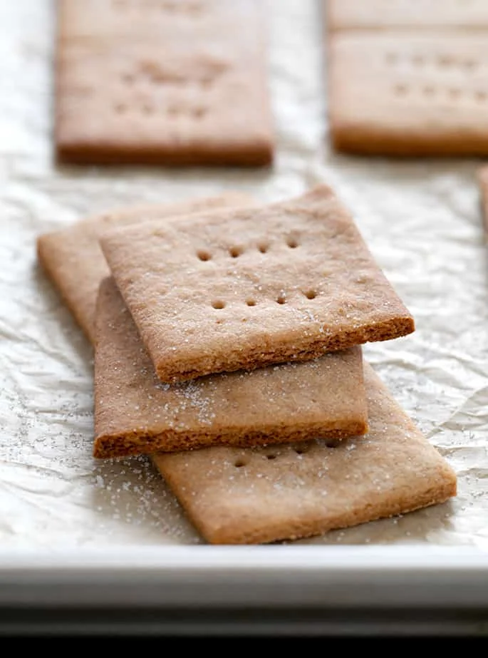 Light brown rectangular graham crackers broken and stacked on metal tray lined in light brown paper