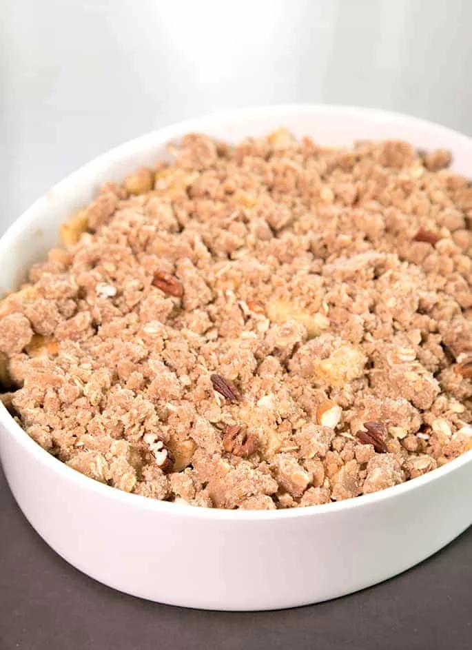 light brown unbaked pieces of crumble topping with a few pecans in a large white casserole dish