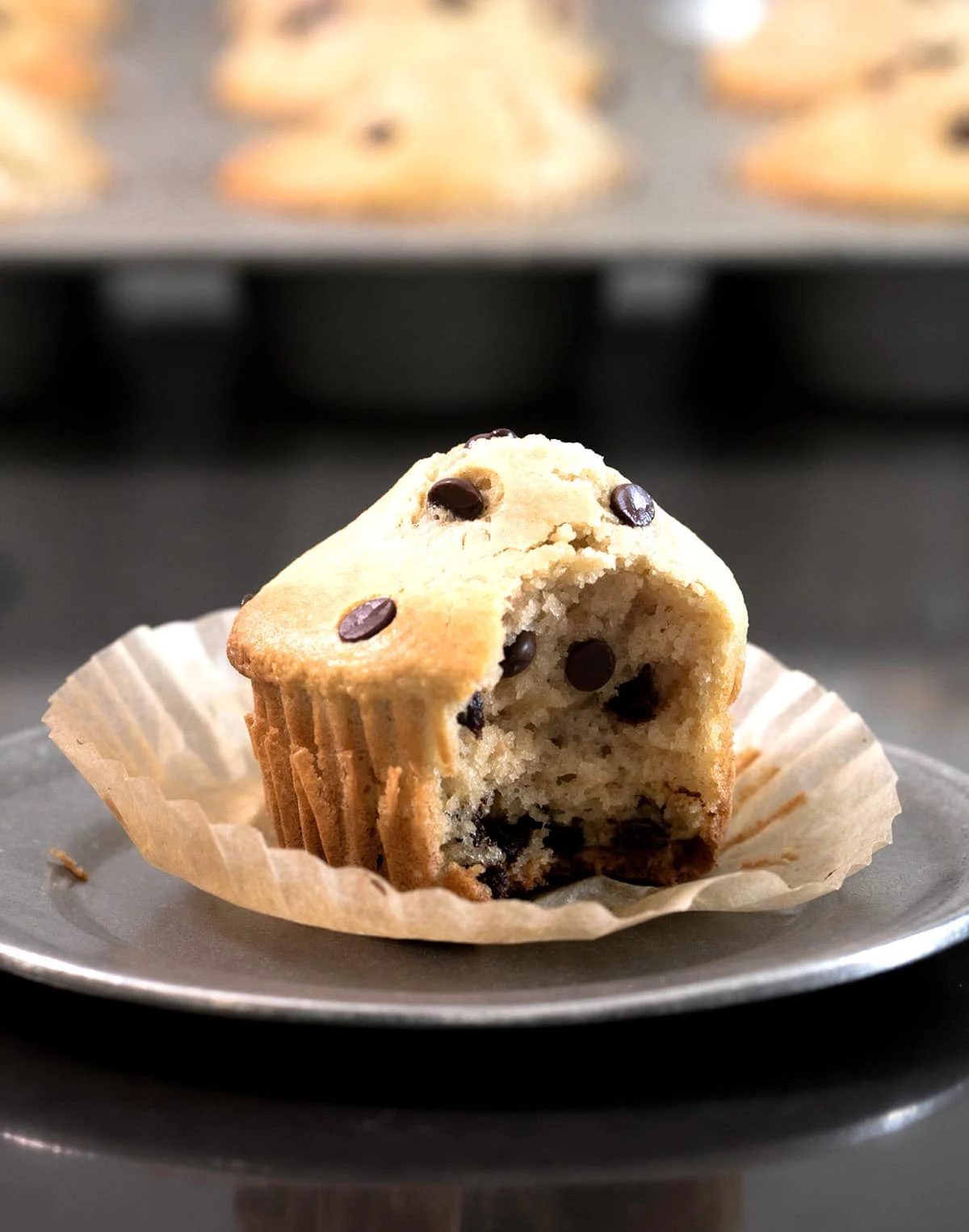light golden brown almond flour muffin with mini chocolate chips with a bite taken with more muffins in tin in background