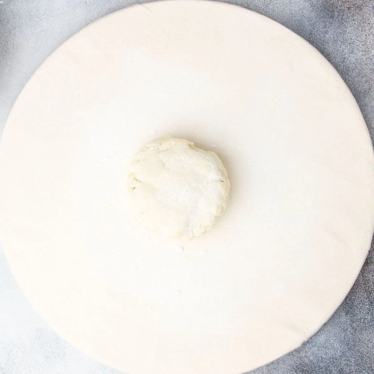 Light tan pie crust disk with white flour sprinkled on top sitting on round light canvas board.