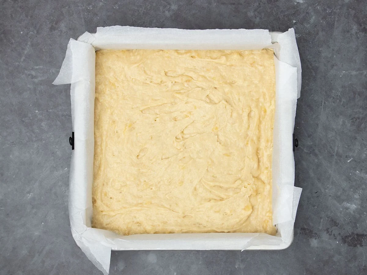 light yellow batter in square baking pan lined with white parchment paper