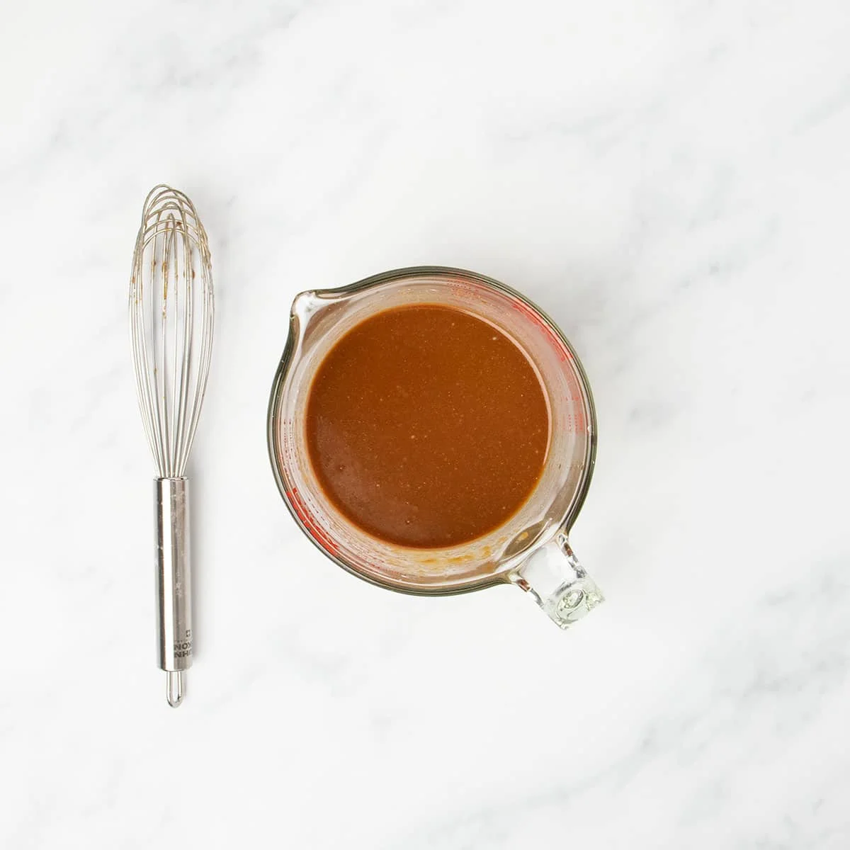 lighter brown liquid gluten free stir fry sauce whisked together in measuring cup with whisk on side