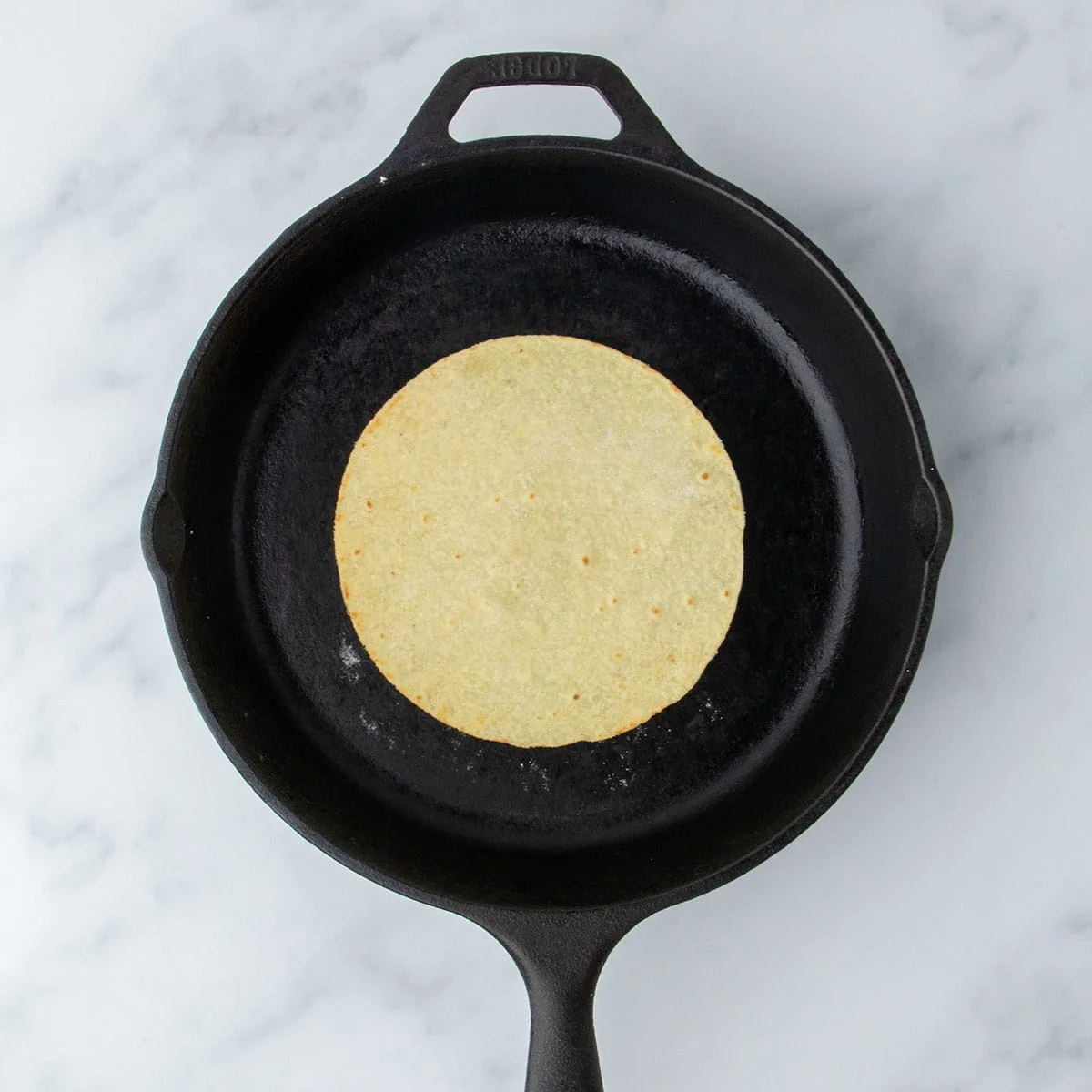 Lightly golden tortilla just after being flipped in skillet.