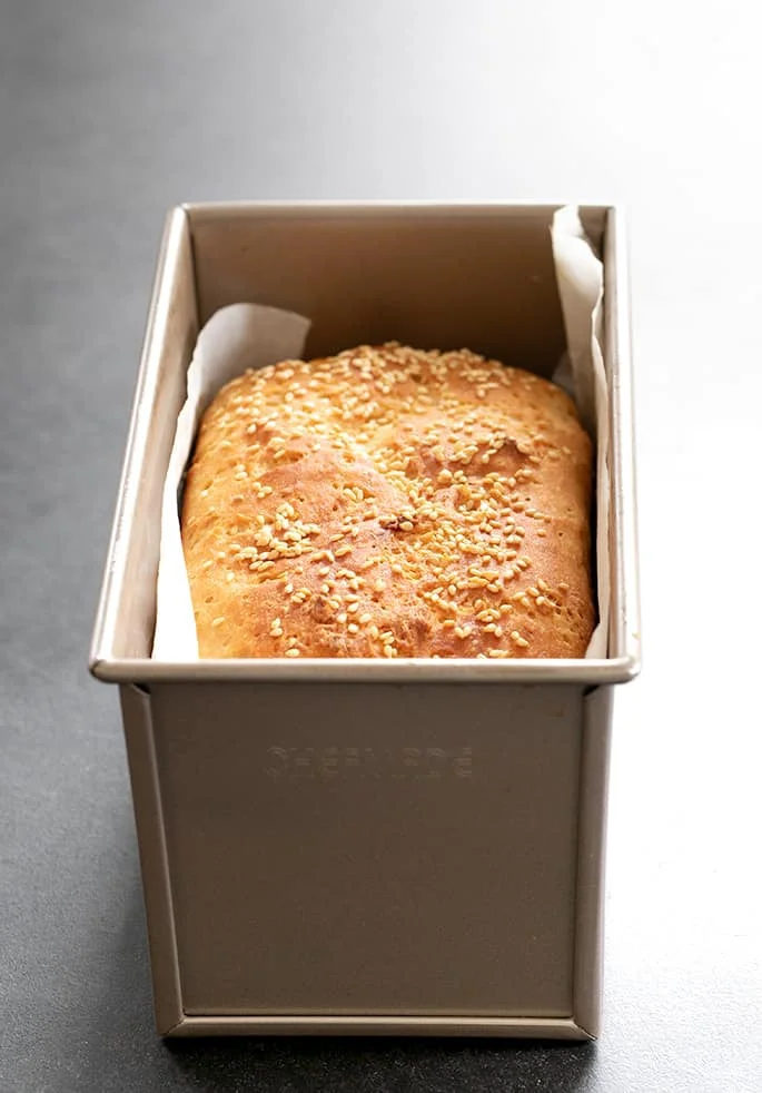 Loaf of bread browned on top with seeds shown baked in pan.