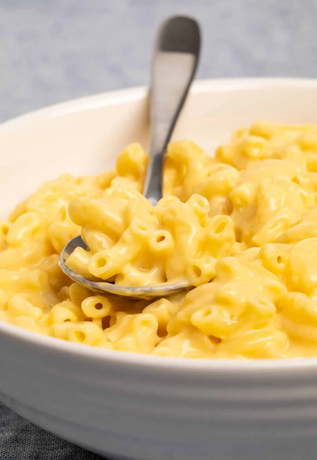 Mac and cheese in wide flat white bowl with metal spoon.