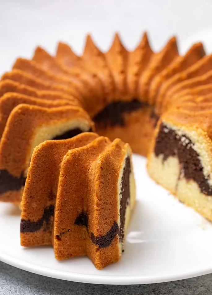 Marble bundt cake on white plate with one slice missing and one slice pulled toward the edge of platter
