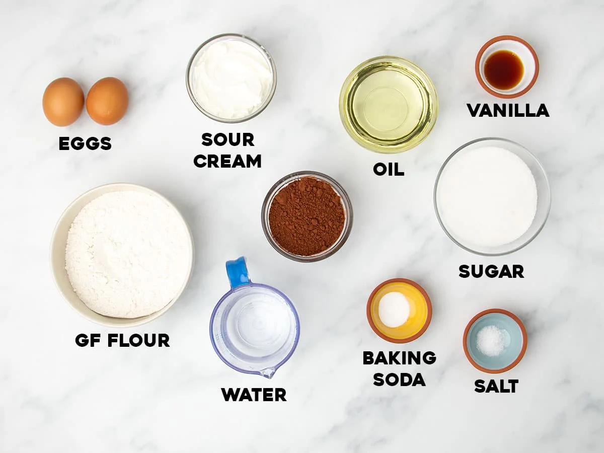 marble surface with ingredients for gluten free chocolate cake in small bowls with black block letters with names of ingredients