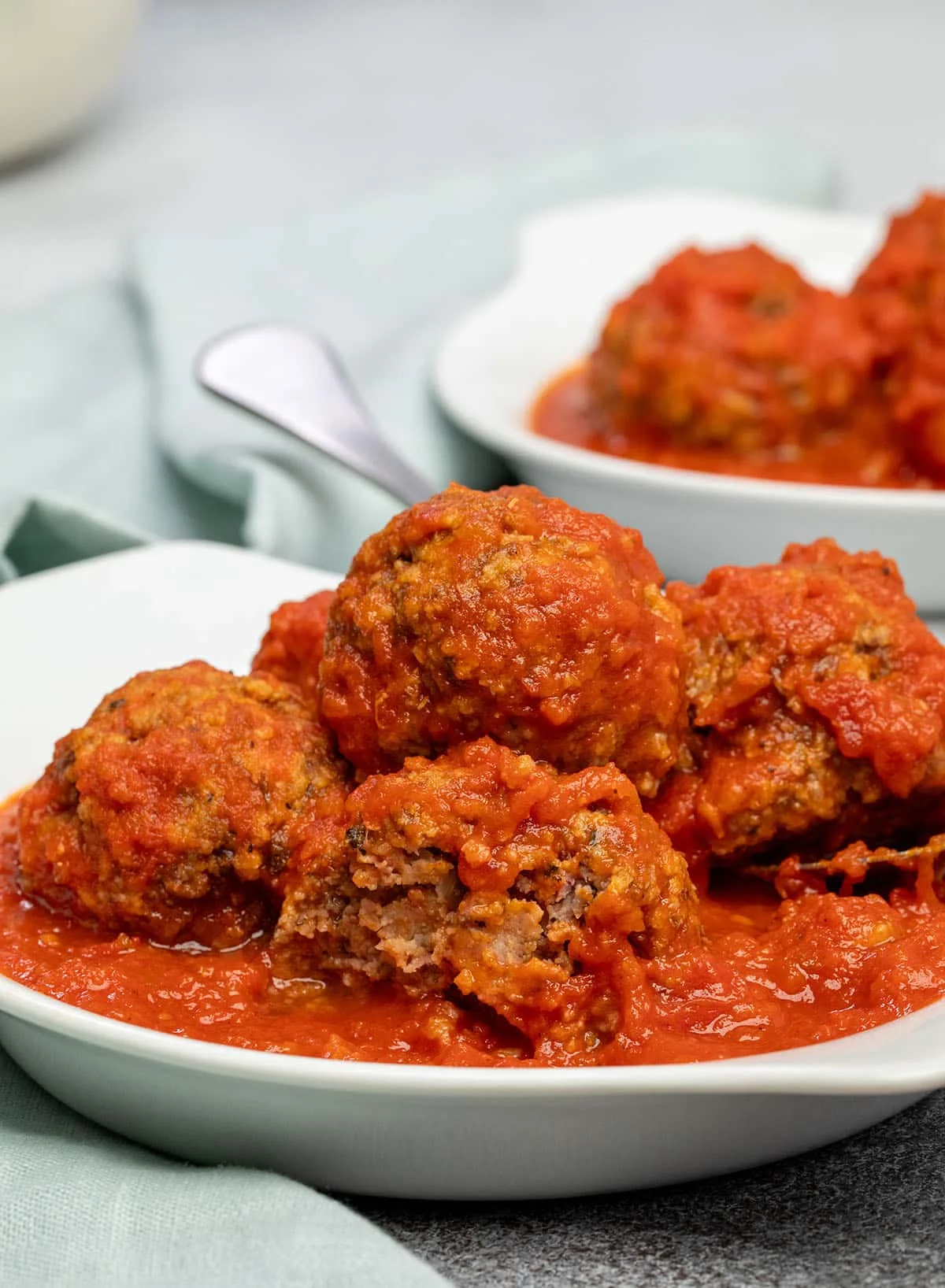 Meatballs in tomato sauce in white dish with one broken in half.