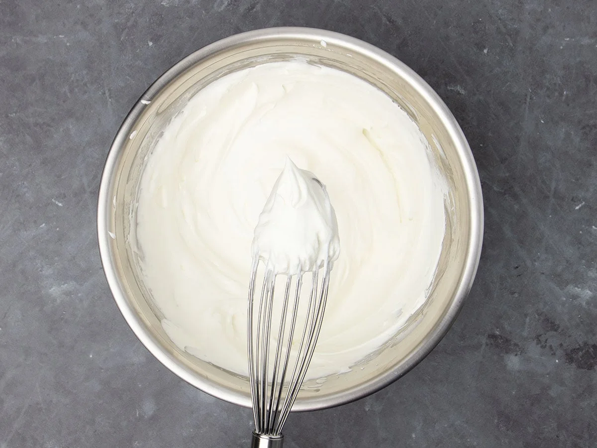 medium-size round metal bowl with white whipped cream in the bowl and some on a wire handheld whisk