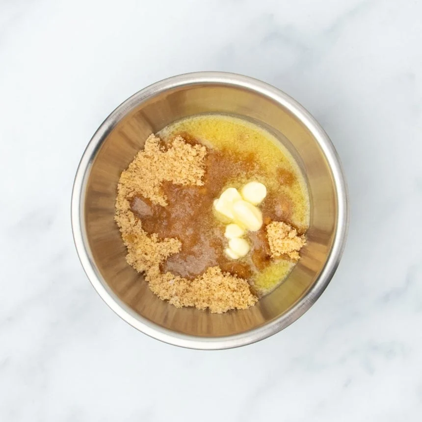 medium-size round metal mixing bowl with yellow melted butter, pale brown sugar, and flour underneath, unmixed