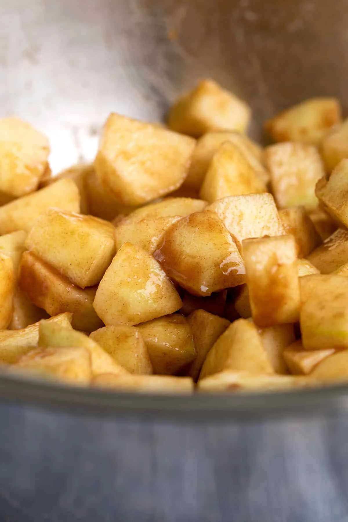 Metal bowl with chunks of raw apples coated in brown sugar.