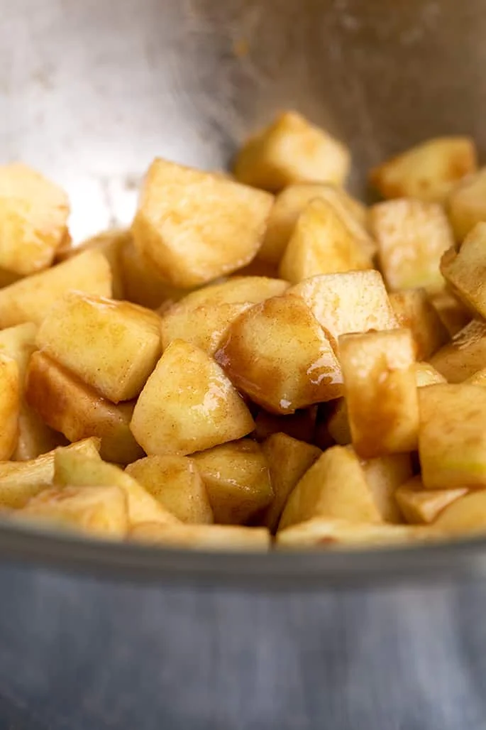 Metal bowl with chunks of raw apples coated in brown sugar