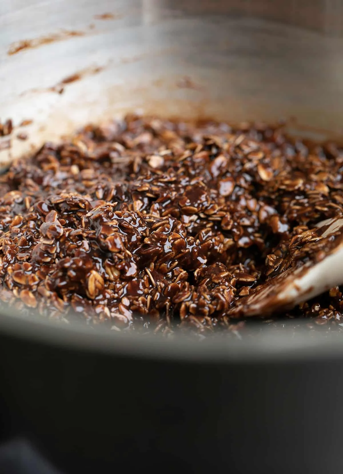 Metal mixing bowl with brown chocolate and oat mixture and a white spatula