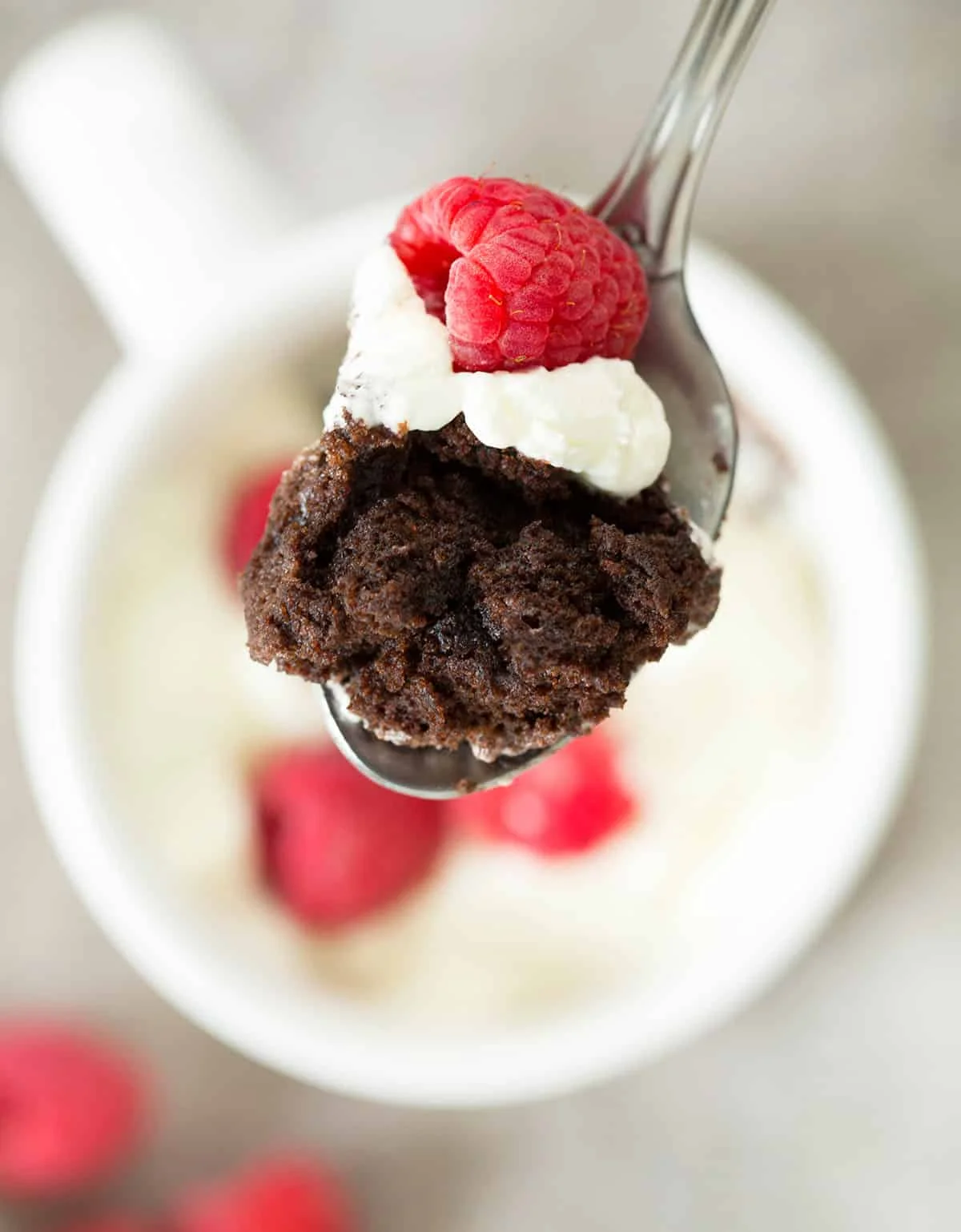Metal spoonful of chocolate cake with whipped cream and raspberry