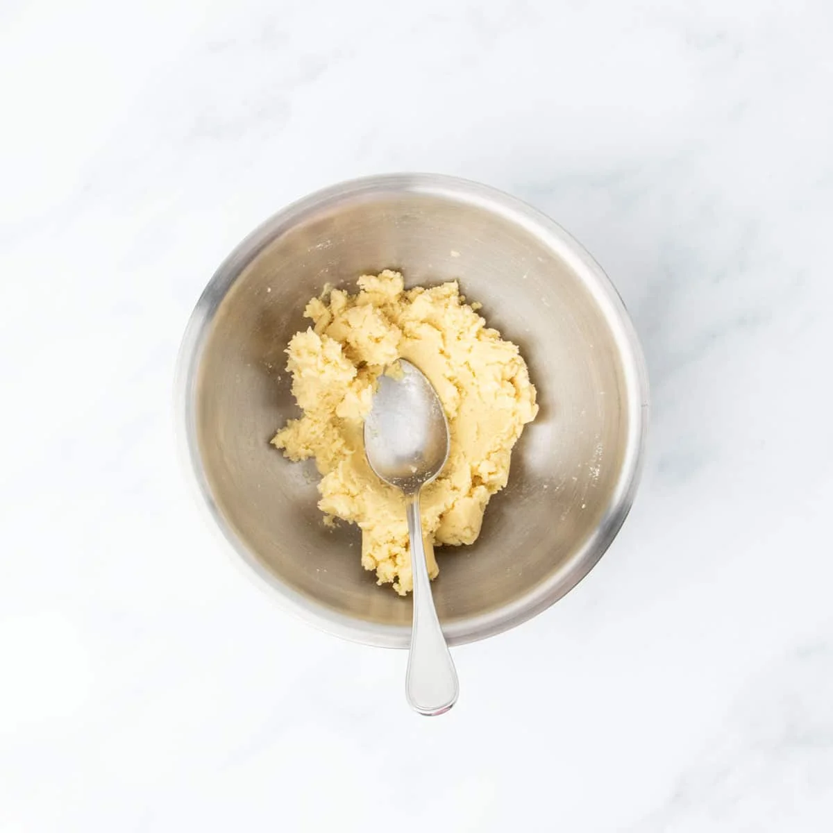 Mixed dough for tortillas in a metal bowl with a spoon.