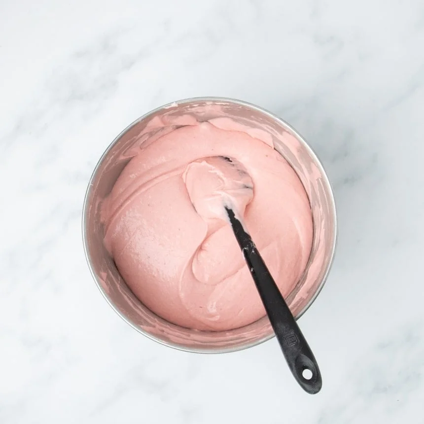 Mixing bowl filled with smooth, pale pink cake batter and a black spatula resting inside.