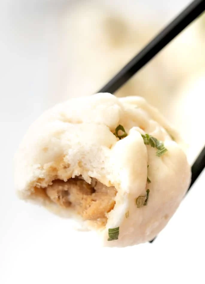 One Chinese meat bun held by chopsticks with a bite taken