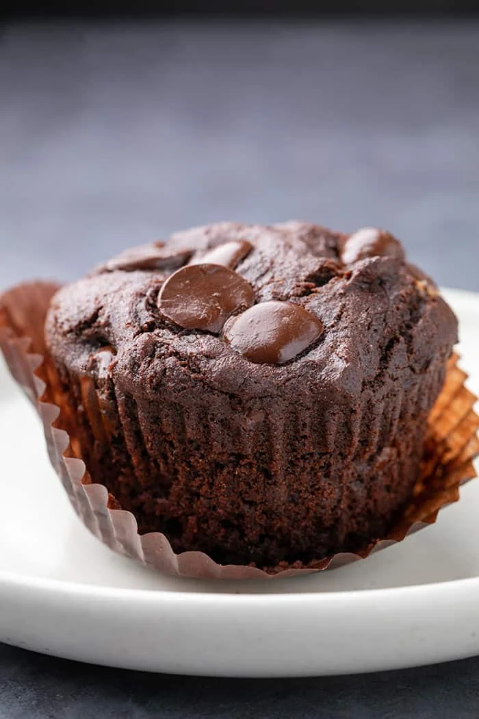 One gluten free chocolate muffin with peeled liner on small white plate