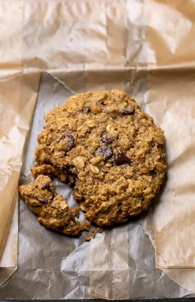 one large broken light brown oatmeal breakfast cookie on a torn white brown wax paper bag