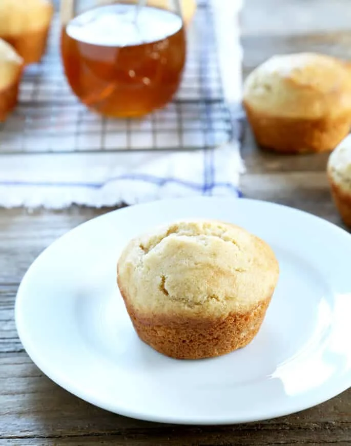 One light brown muffin on a small white plate on a brown wood table.